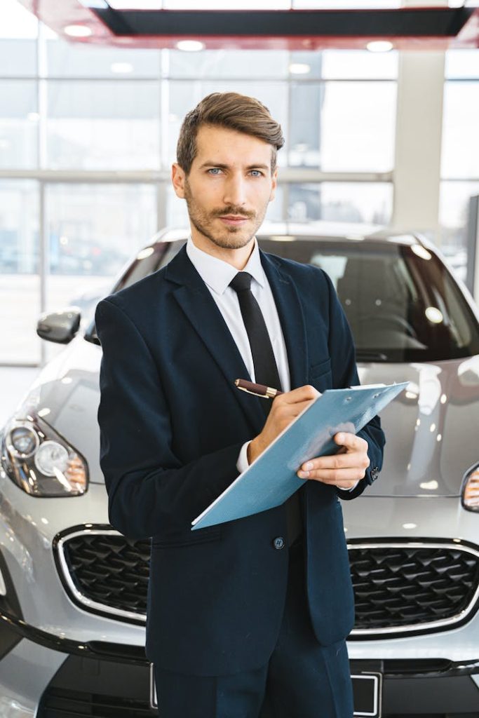 Sales professional in a suit holding a clipboard in dealership showroom, showcasing cars.
