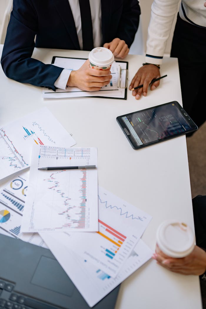High-angle view of office meeting with charts, coffee, and tablet device.